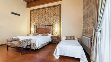A hotel room with two beds, a wooden ceiling, a stone wall, and a radiator.