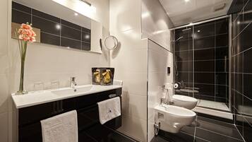 Un baño moderno con diseño de baldosas blanco y negro, un espejo grande, cabina de ducha de cristal y un florero con flores en el tocador.