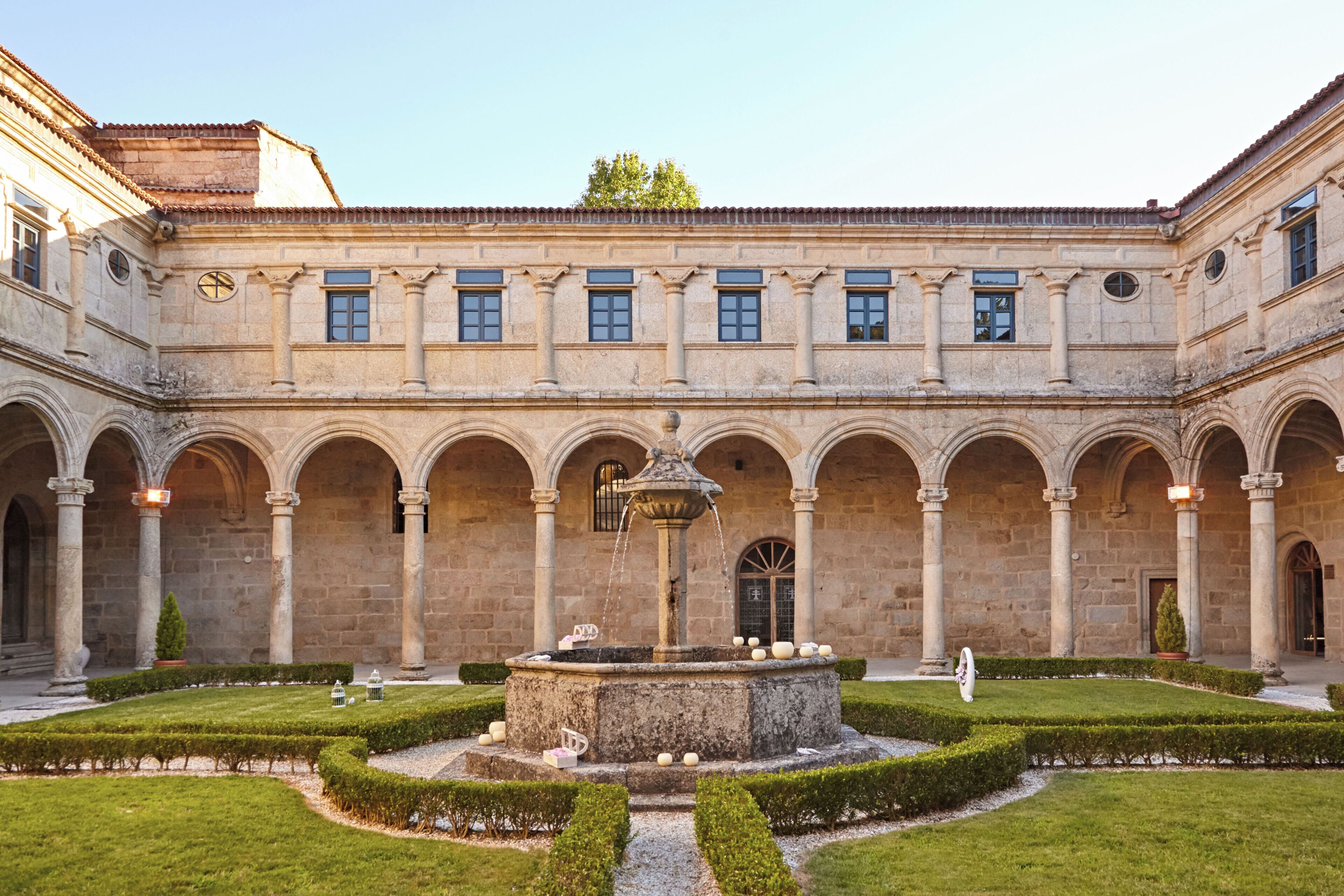 A courtyard with a central fountain, surrounded by a symmetrical garden and a building with multiple arches and windows.