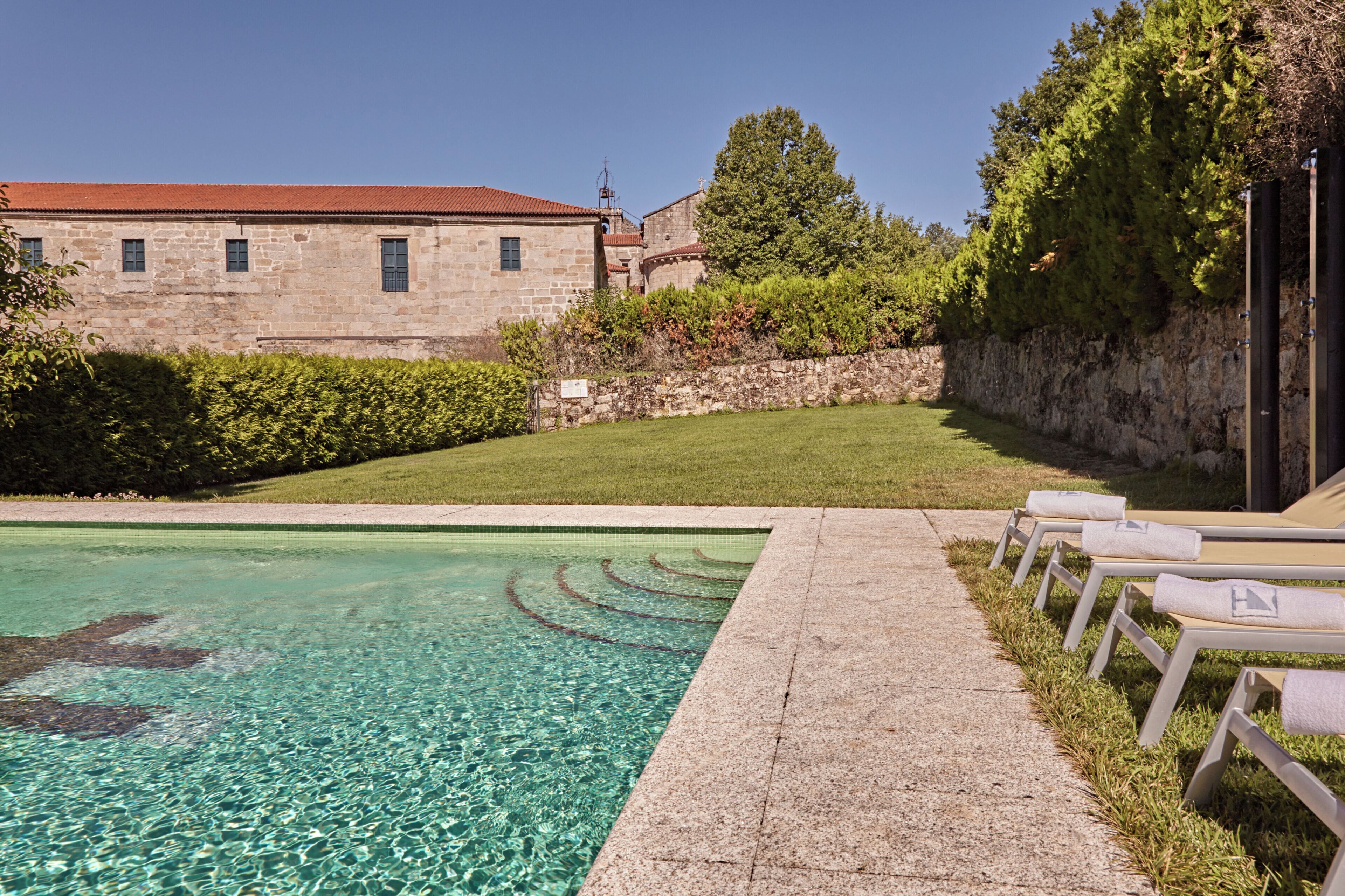 A clear swimming pool with lounge chairs, a stone building, and a well-maintained lawn.