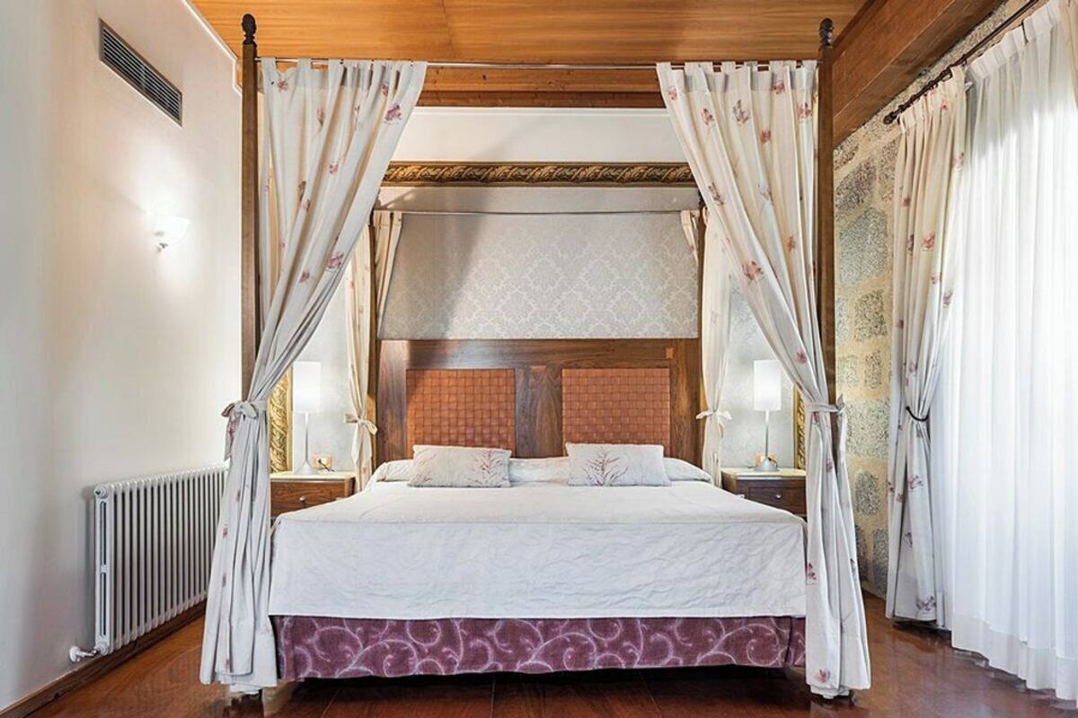 A four-poster canopy bed with a wooden headboard, white bedding, and floral curtains.