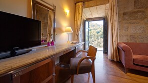 A hotel room with a TV, a desk with a lamp, a chair, a sofa, and a view of the outdoors. - Eurostars Monumento Monasterio de San Clodio Hotel (Leiro)