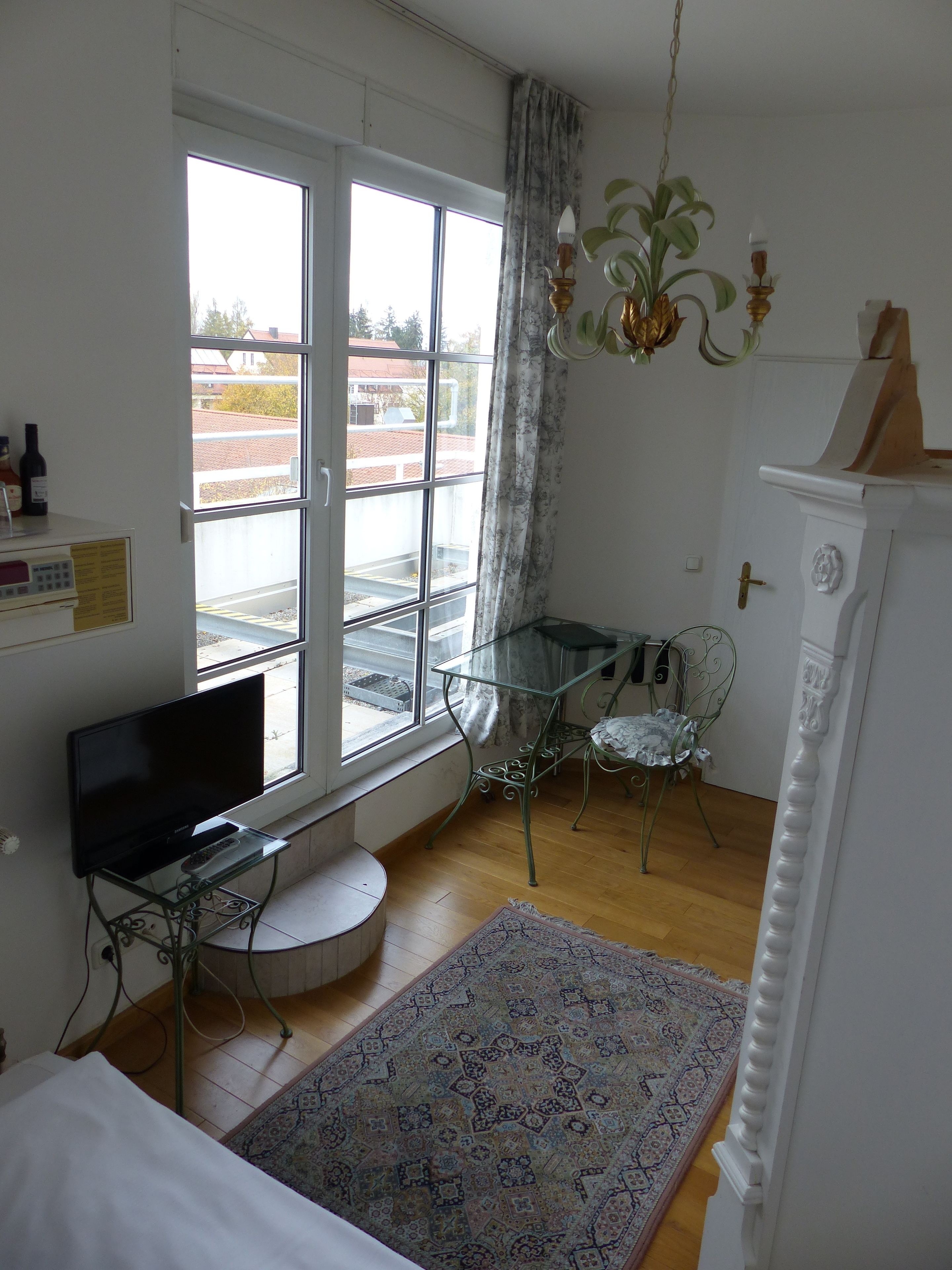 Una habitación con un ventanal grande, un televisor de pantalla plana, una mesa de vidrio, una alfombra estampada y un armario blanco.