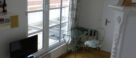 Una habitación con un ventanal grande, un televisor de pantalla plana, una mesa de vidrio, una alfombra estampada y un armario blanco.