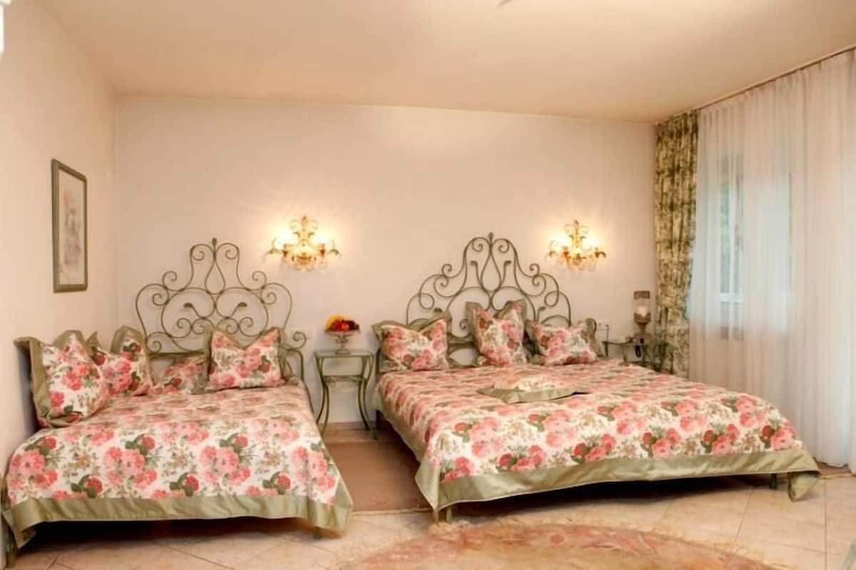 A bedroom with two beds, floral bedding, wall sconces, and a view of a garden.