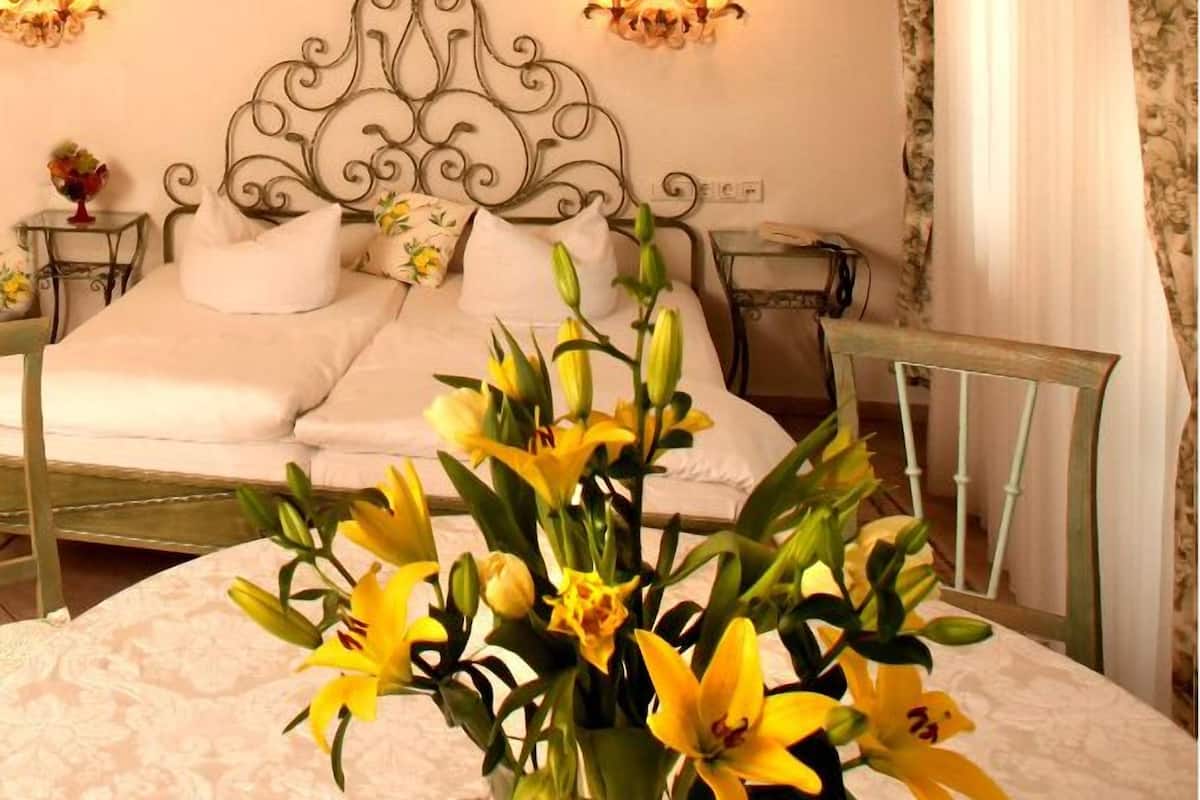 A bedroom with a bed, two bedside tables, a chandelier, and a vase of flowers.