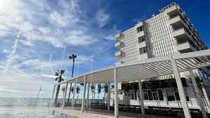 A modern hotel with a geometric facade, a covered outdoor area with a water feature, and a view of the sea. - Fay Victoria Beach (Rincon de la Victoria)