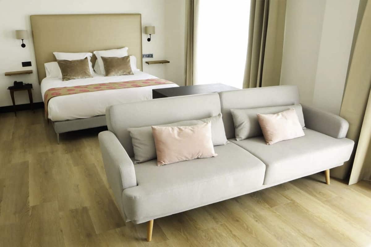 A hotel room with a bed, two sofas, a nightstand, and a lamp.