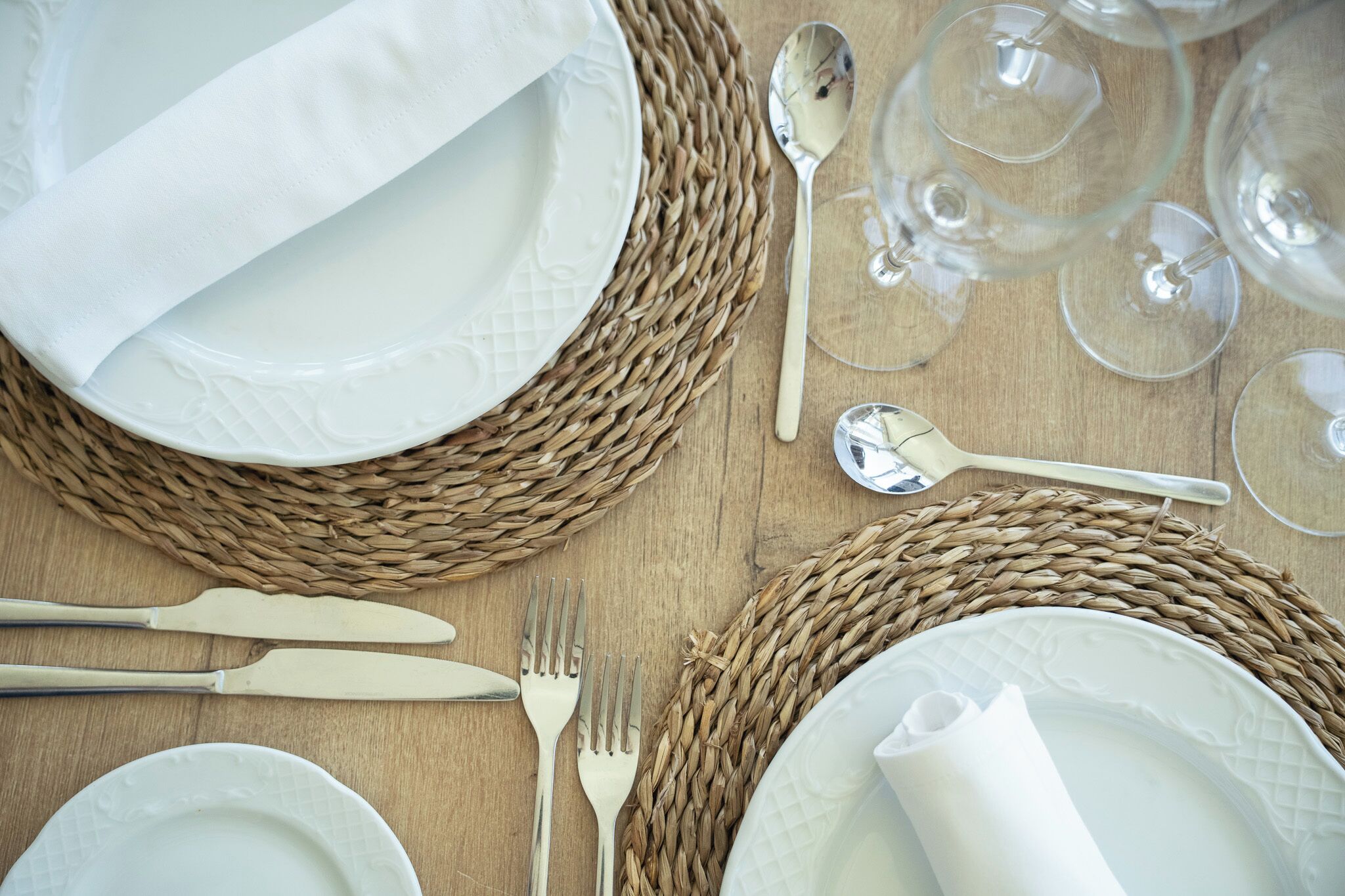 A table set with white plates, cutlery, and glasses on a woven placemat.