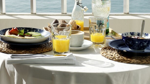 A table set with breakfast items, including fruit, bread, and beverages, overlooking a body of water. - Fay Victoria Beach (Rincon de la Victoria)
