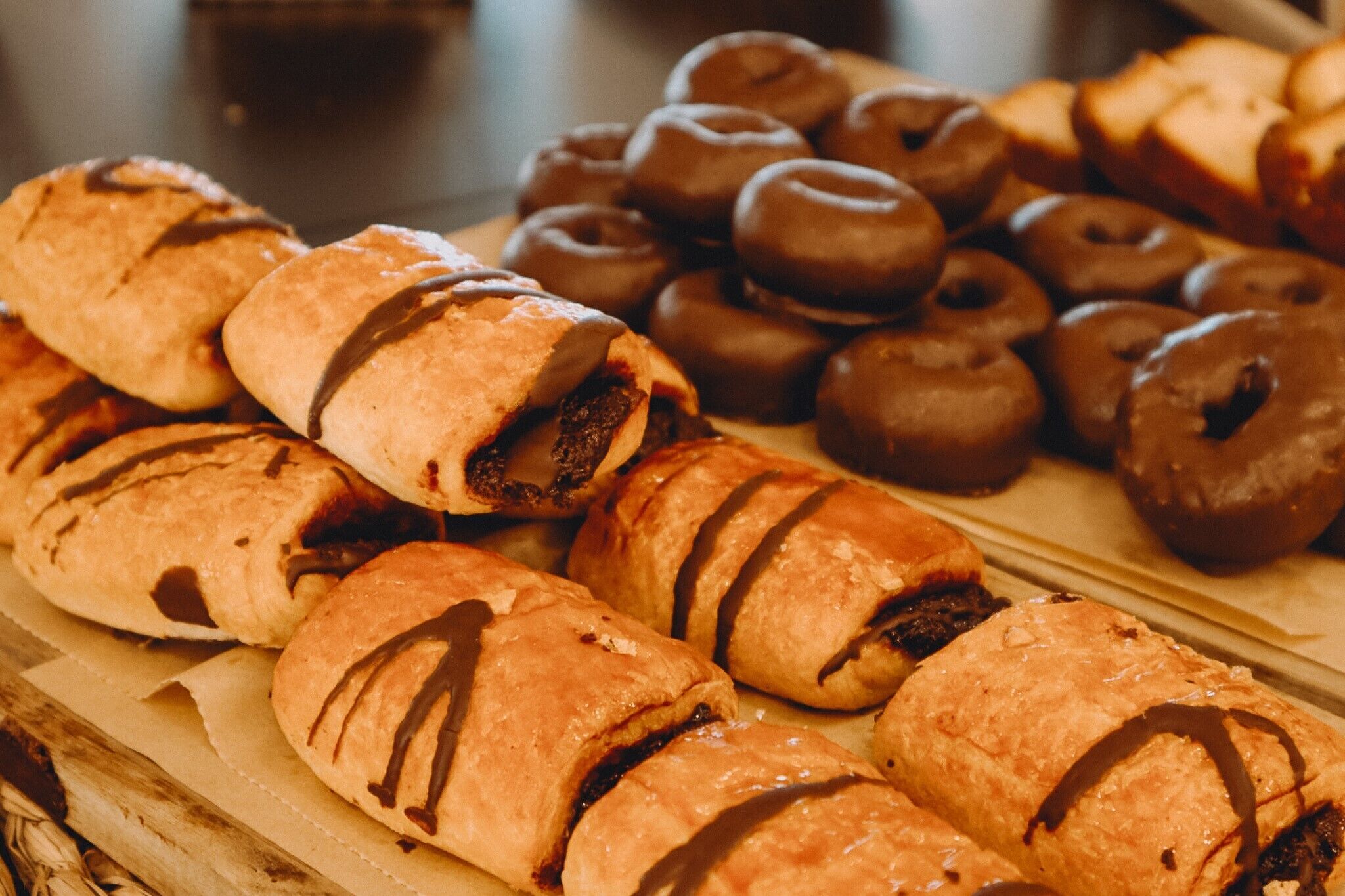 A variety of pastries, including chocolate-covered and filled doughnuts, arranged on a wooden board.