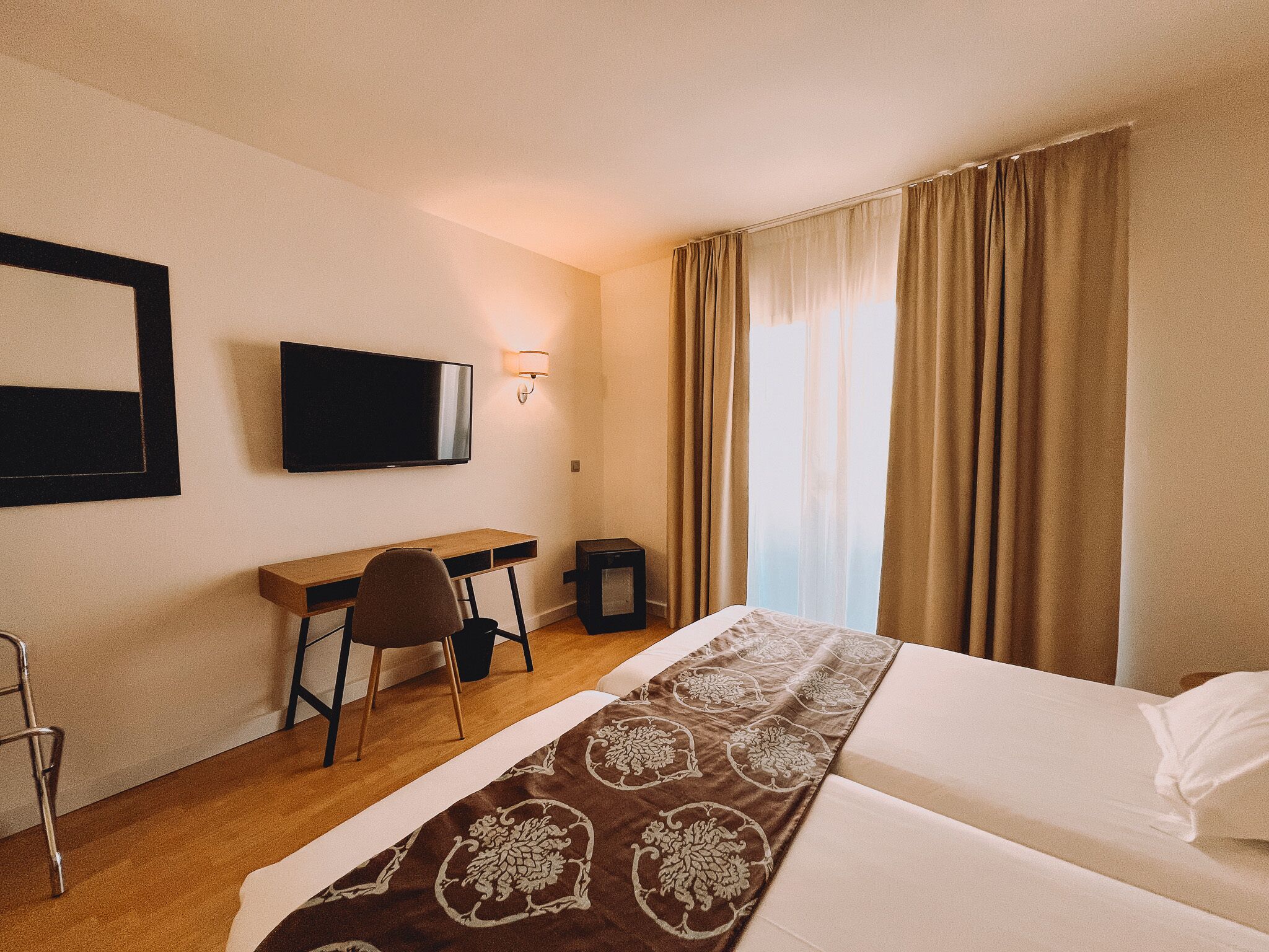 A hotel room with a bed, a desk, a chair, a television, and a window with curtains.