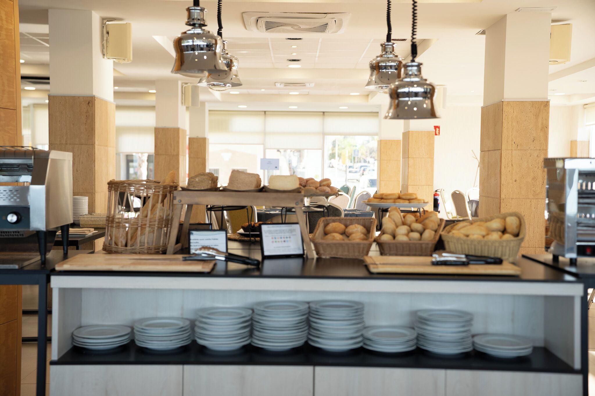 A breakfast buffet area with bread baskets, plates, and a coffee machine.