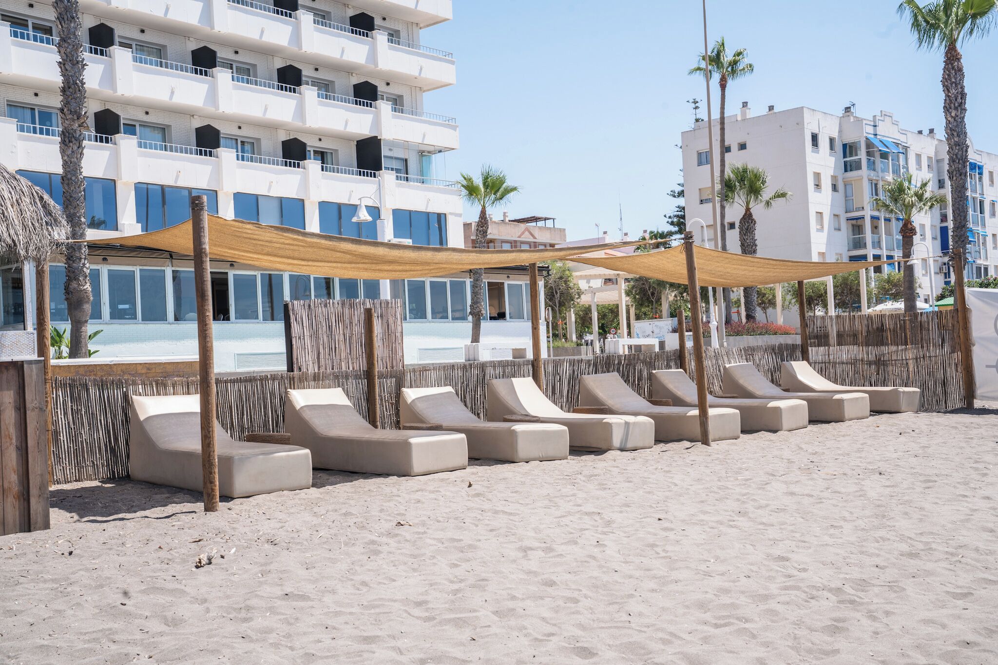Un hotel frente a la playa con tumbonas, piscina y palmeras.