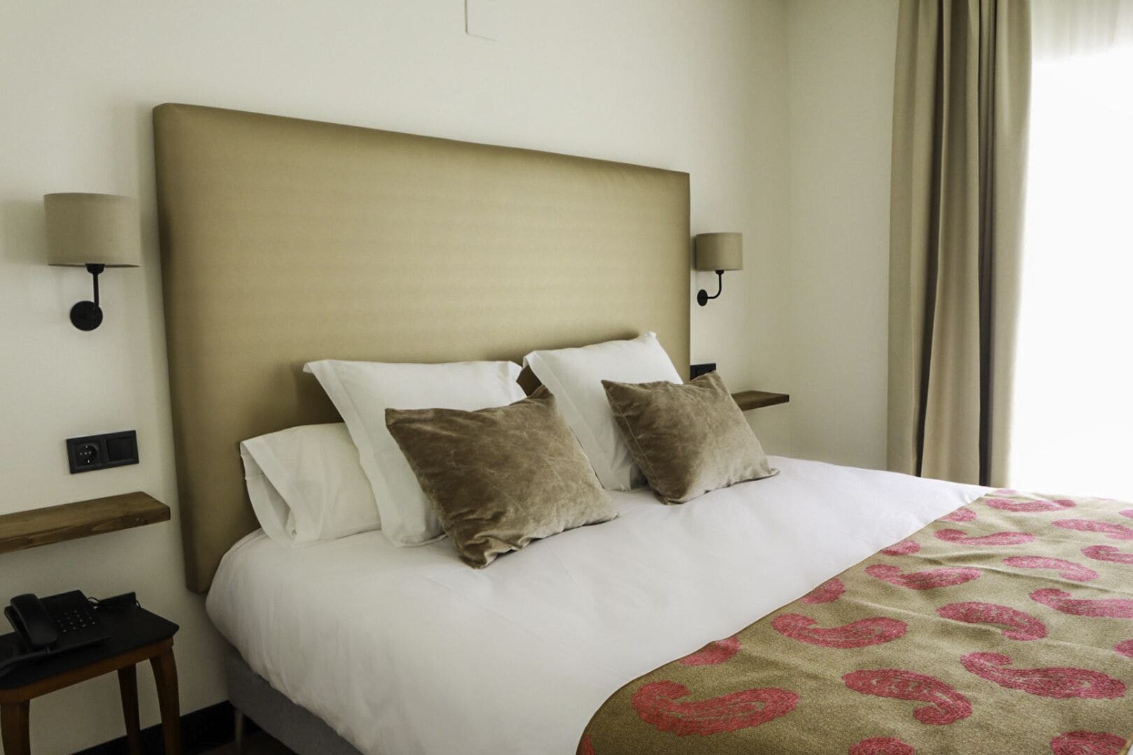 A hotel room with a large bed, two bedside tables, a telephone, and a lamp on each side.