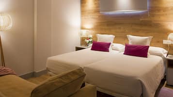 Habitación de hotel con dos camas, un cabecero de madera, una mesita de noche con lámpara y una silla.
