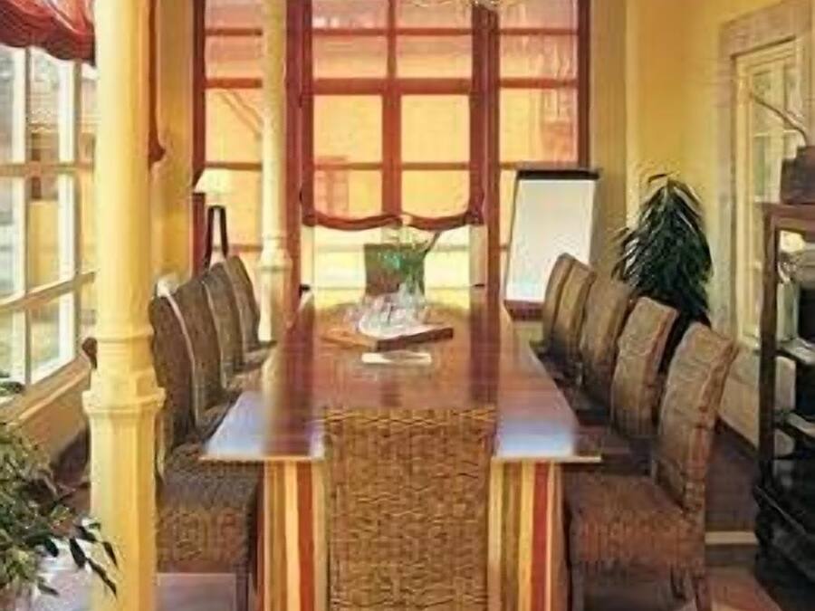Un comedor con una mesa larga, sillas con cojines y una araña.