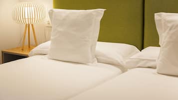 A neatly made bed with white bedding and pillows, a wooden bedside table with a lamp, and a green headboard.