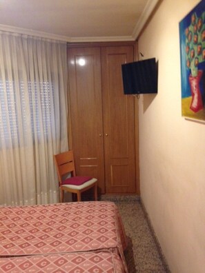 Quarto com cama, cadeira, guarda-roupa, um quadro e televisão na parede.