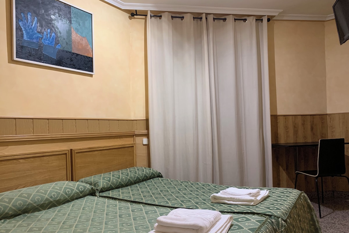 A hotel room with two beds, a painting on the wall, a curtain, and a chair.