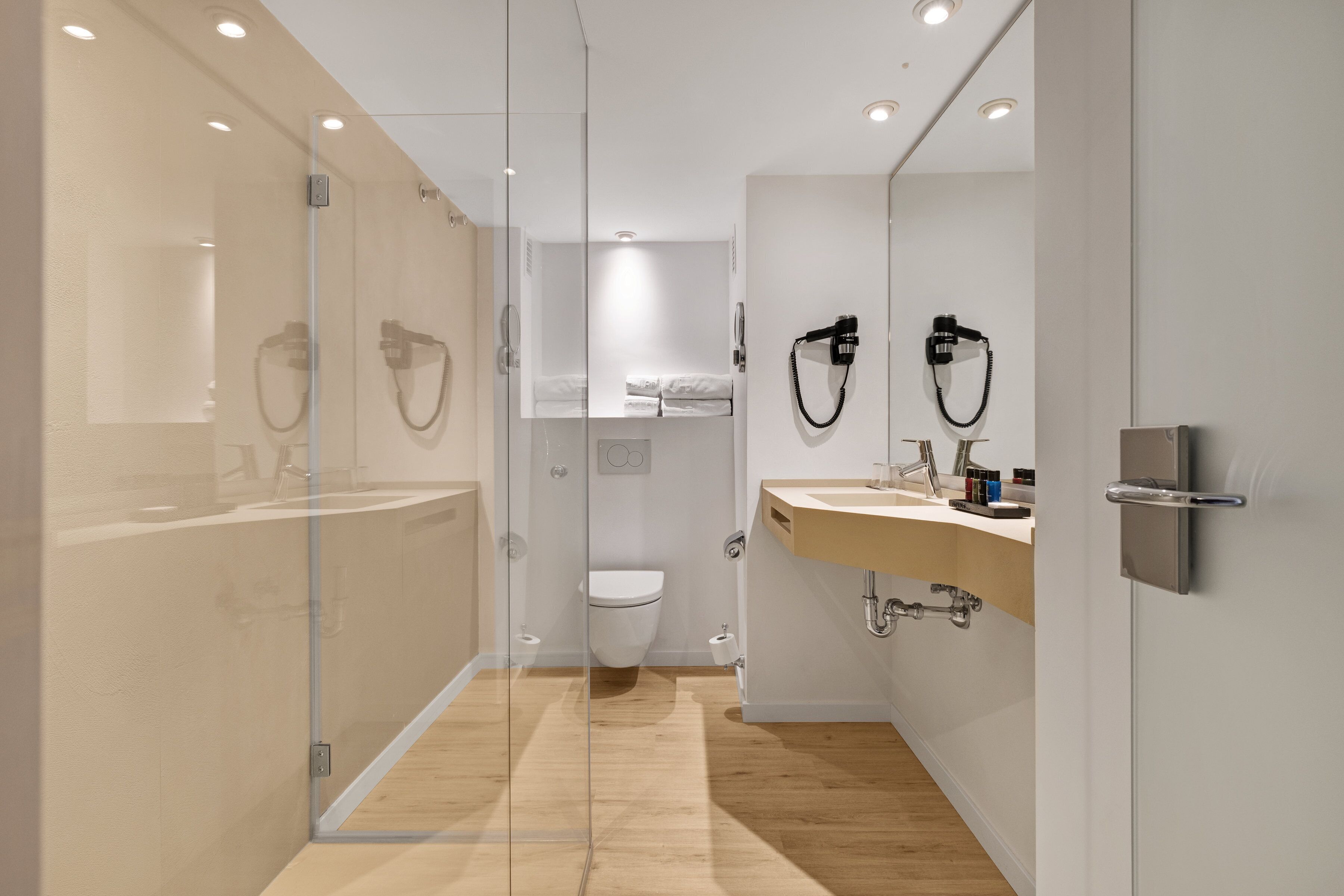 A modern bathroom with a glass shower enclosure, a toilet, and a vanity with a sink and towel rack.