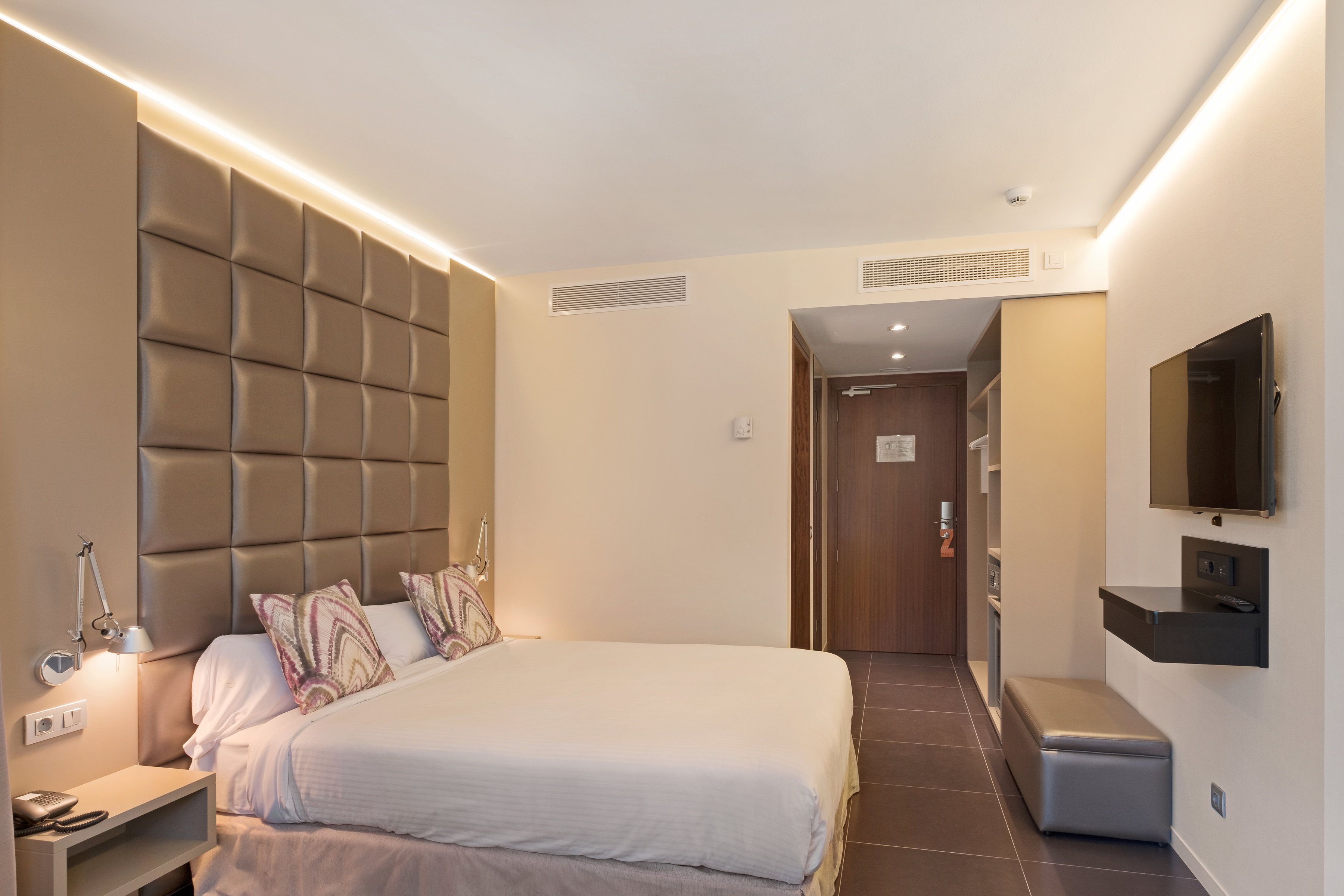 A modern hotel room with a large bed, bedside table, lamp, and a mounted TV.