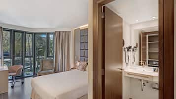 Una habitación de hotel moderna con una cama grande, un escritorio, una silla y un baño con tocador y espejo.