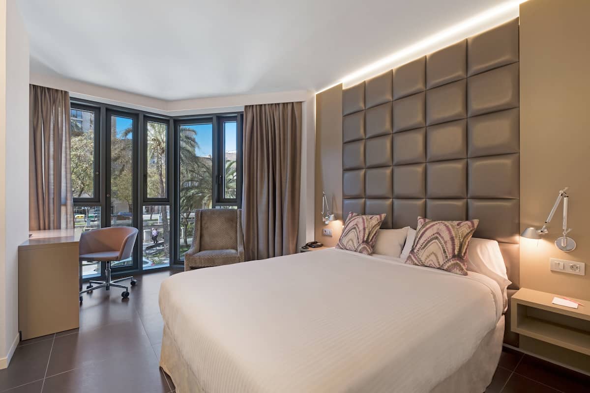 A hotel room with a large bed, a desk, a chair, and a view of the outdoors.