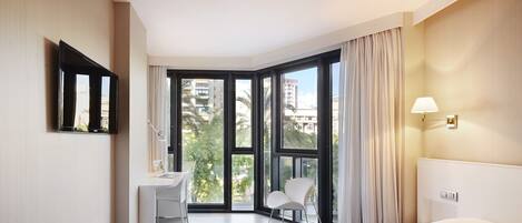 Habitación de hotel moderna con una cama grande, un escritorio, una silla y vistas de la ciudad a través de amplios ventanales.