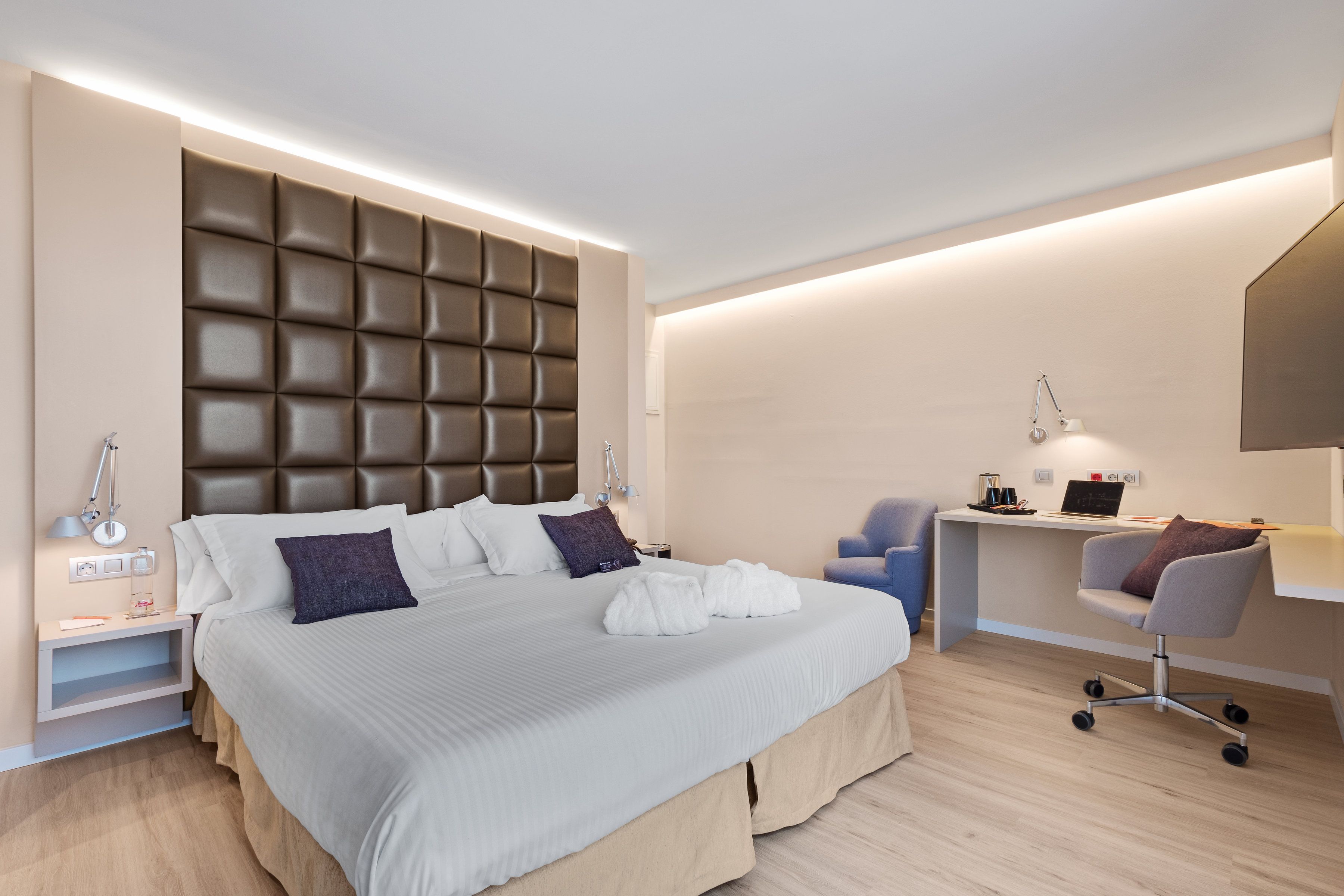 A modern hotel room with a large bed, a desk, and a chair.