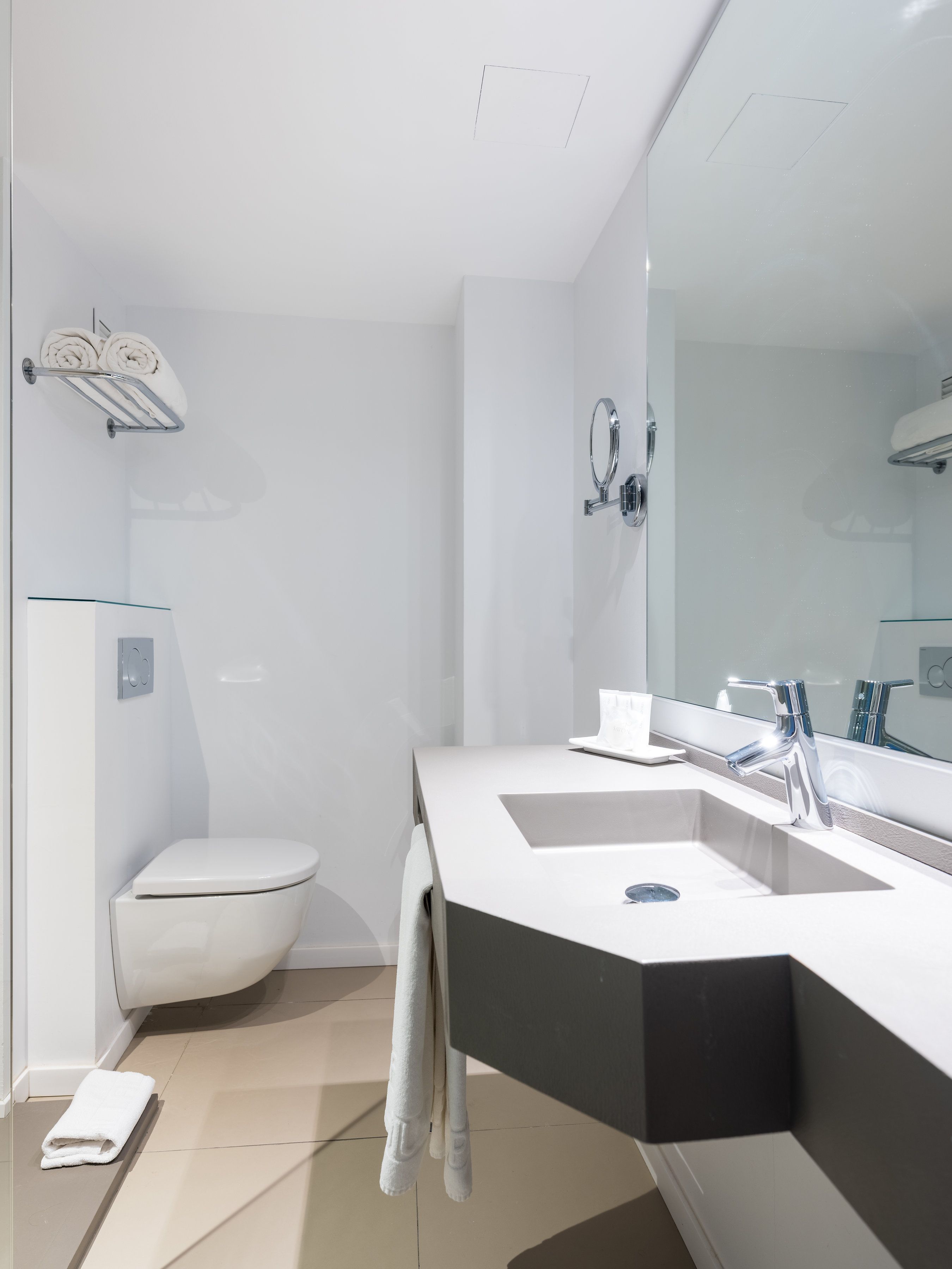 Et moderne badeværelse med en hvid vask, et stort spejl og et toilet.