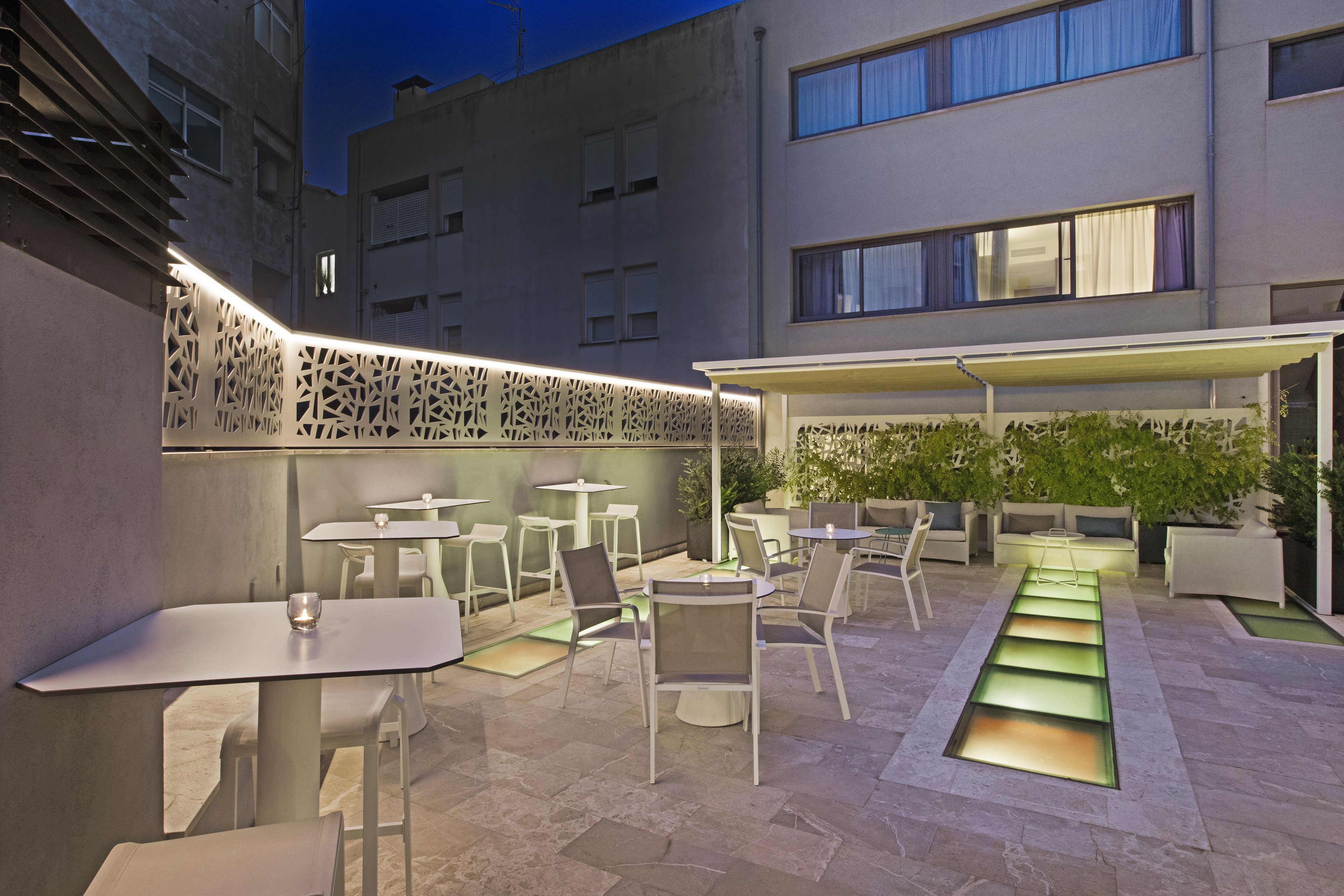 An outdoor patio area with multiple tables and chairs, a decorative wall, and a seating area with cushions.