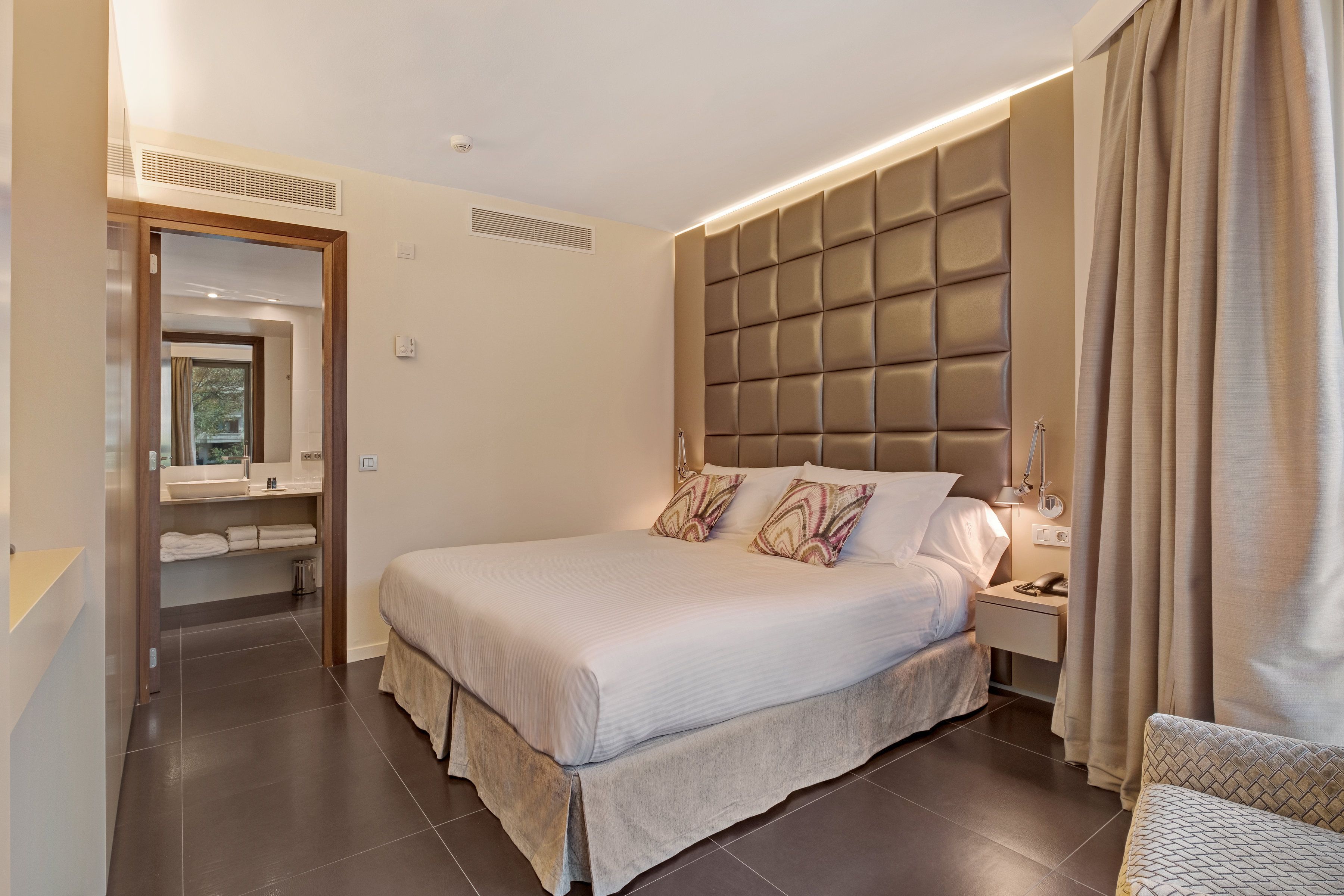 A modern bedroom with a large bed, a nightstand, a bedside table, a built-in headboard, and a walk-in closet.