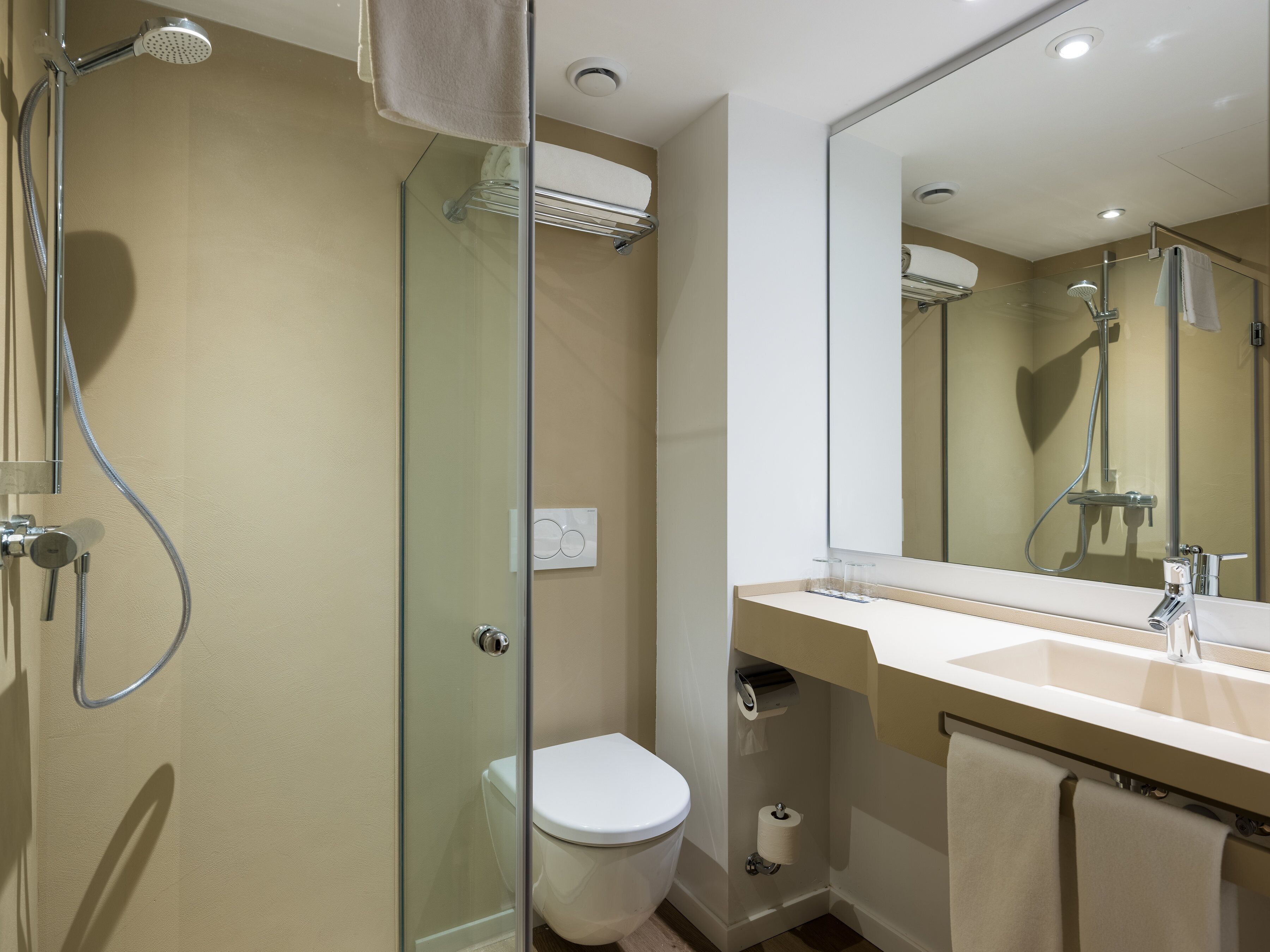 Un baño moderno con ducha de vidrio, inodoro blanco y tocador con espejo.