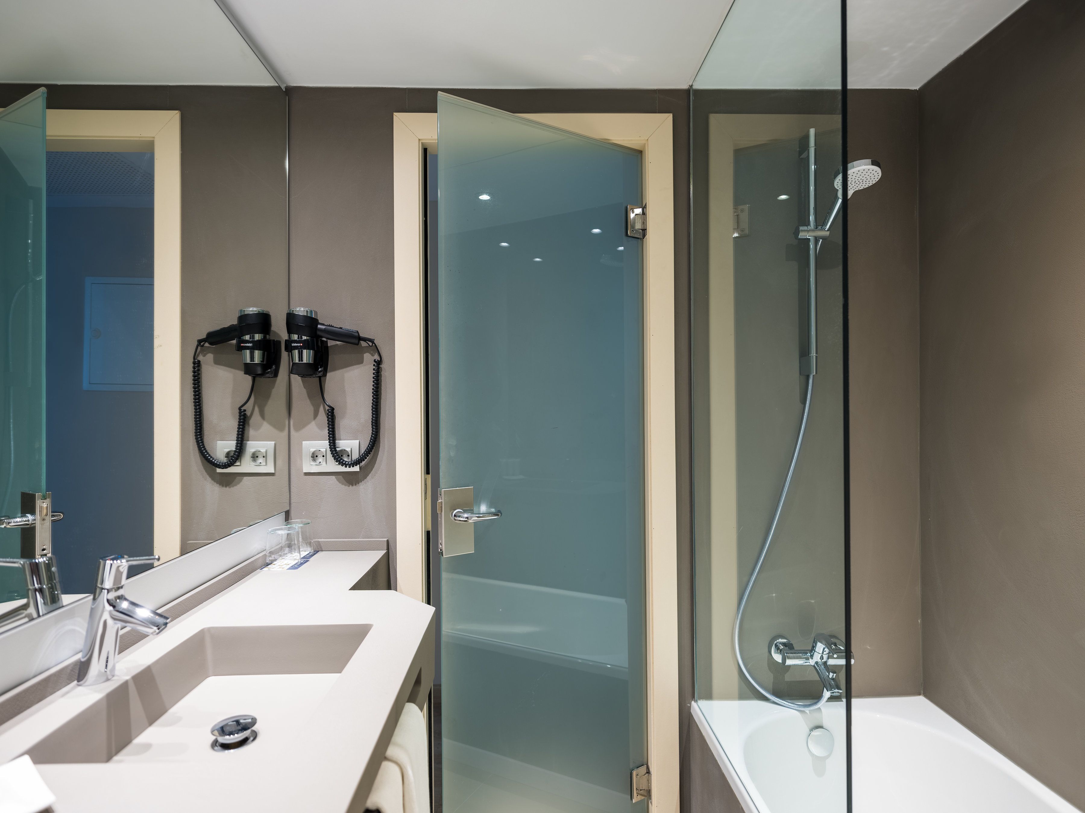 Une salle de bain moderne dotée d’une douche à parois de verre, d’un meuble-lavabo à deux vasques et d’un sèche-cheveux fixé au mur.