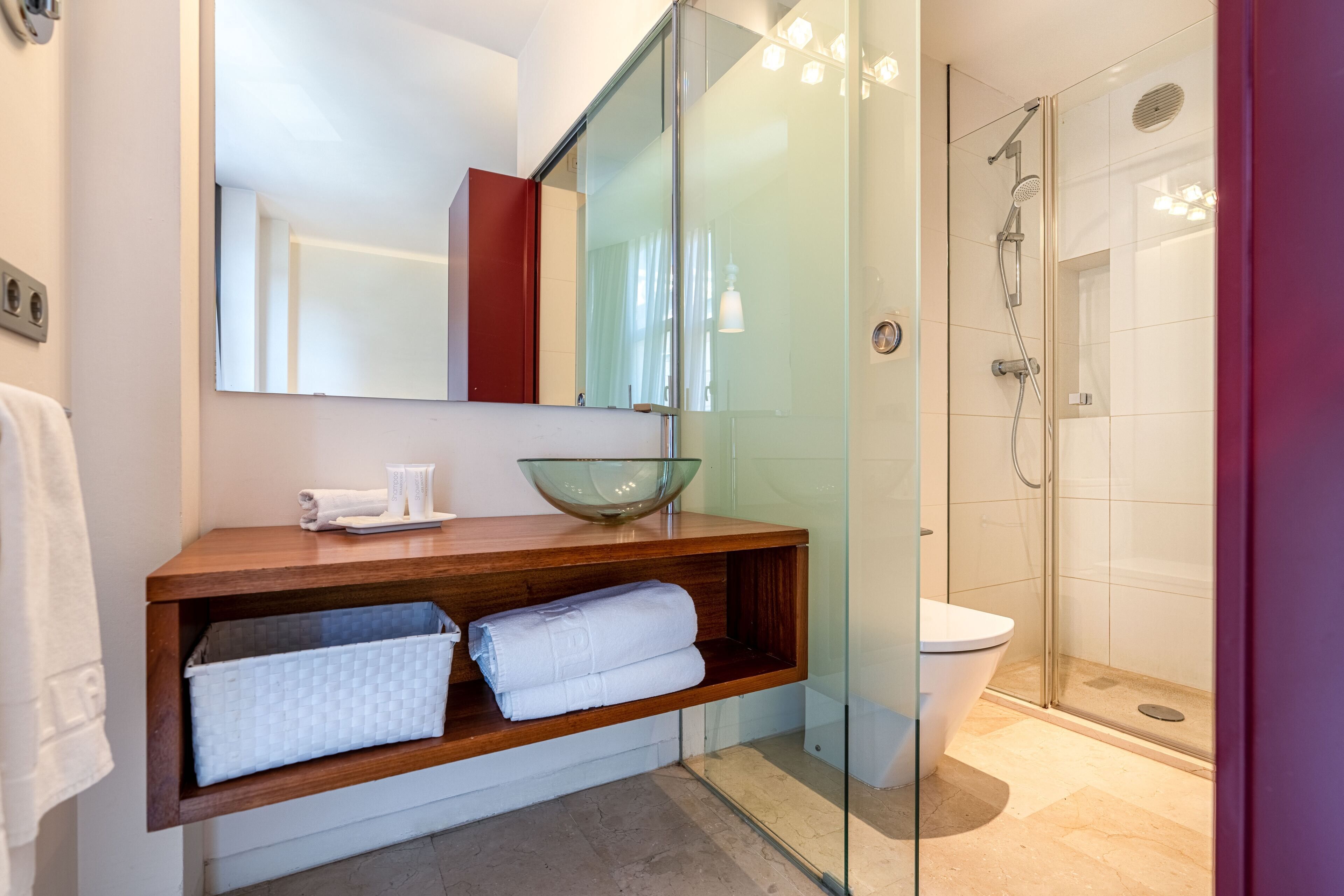 Une salle de bain moderne avec une douche à parois de verre, un meuble-lavabo en bois doté d’un vasque en verre, et un grand miroir.