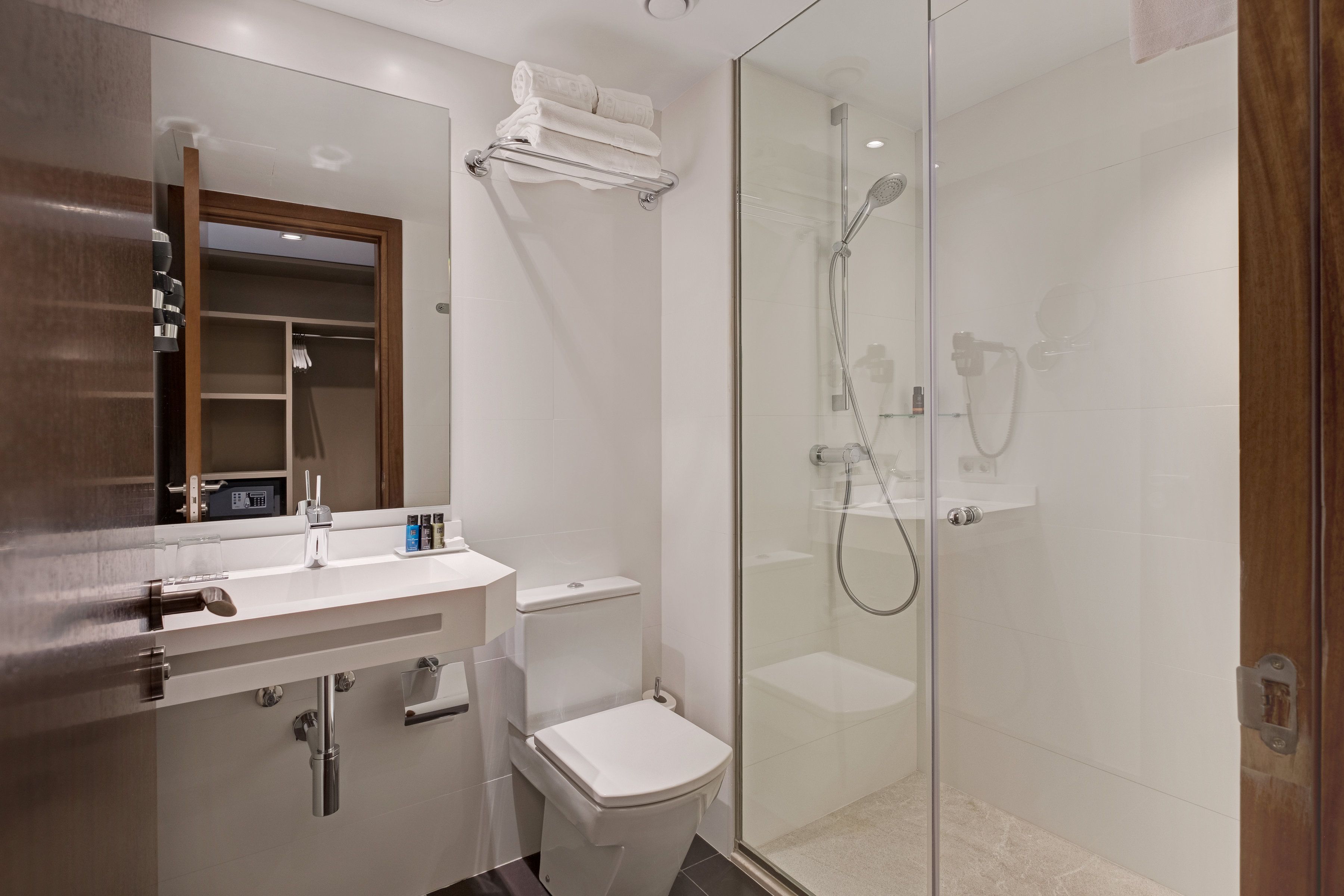 A modern bathroom with a glass-enclosed shower, a white toilet, and a vanity with a mirror and towel rack.