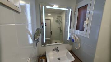 A bathroom with a white sink, a mirror with lights, a handheld showerhead, and a hairdryer.
