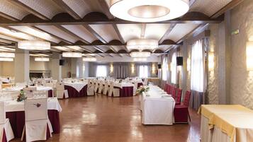 Une salle de banquet avec des tables rondes, des nappes blanches et des chaises rouges.