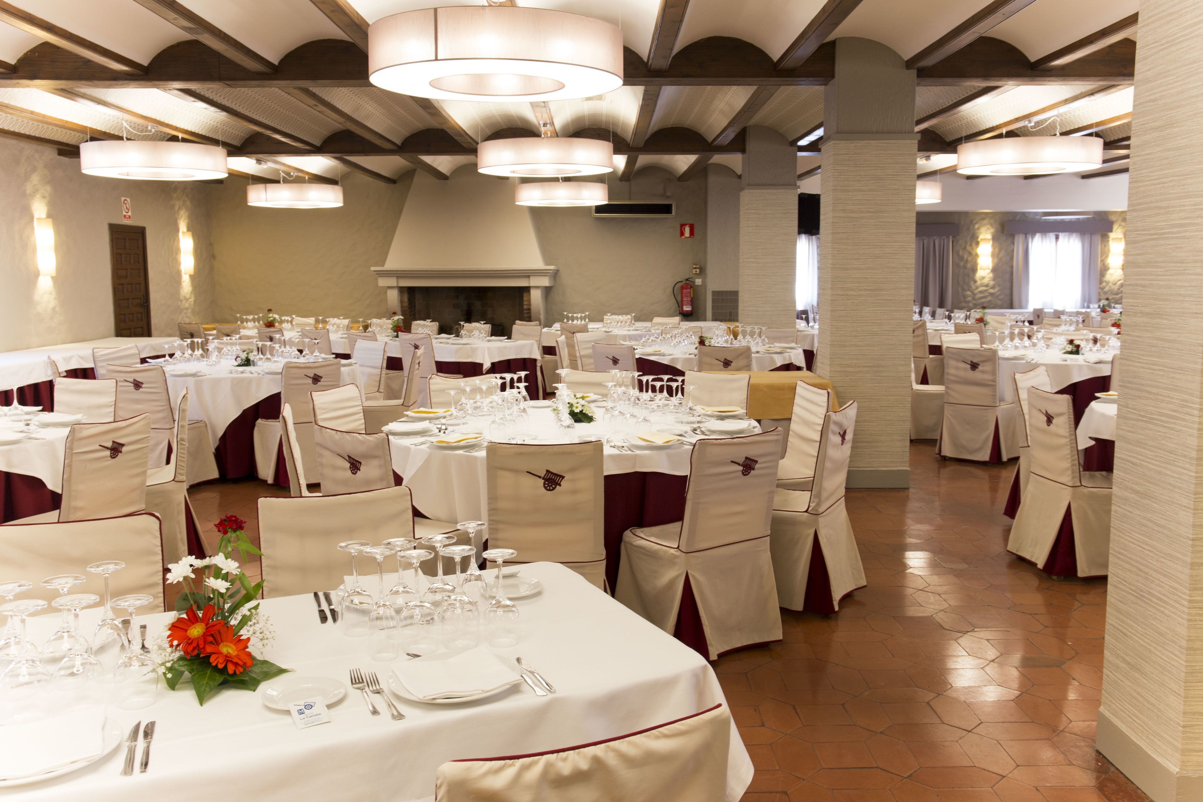 Une salle de banquet avec des tables rondes, des nappes blanches et des chaises ornées de rubans rouges.