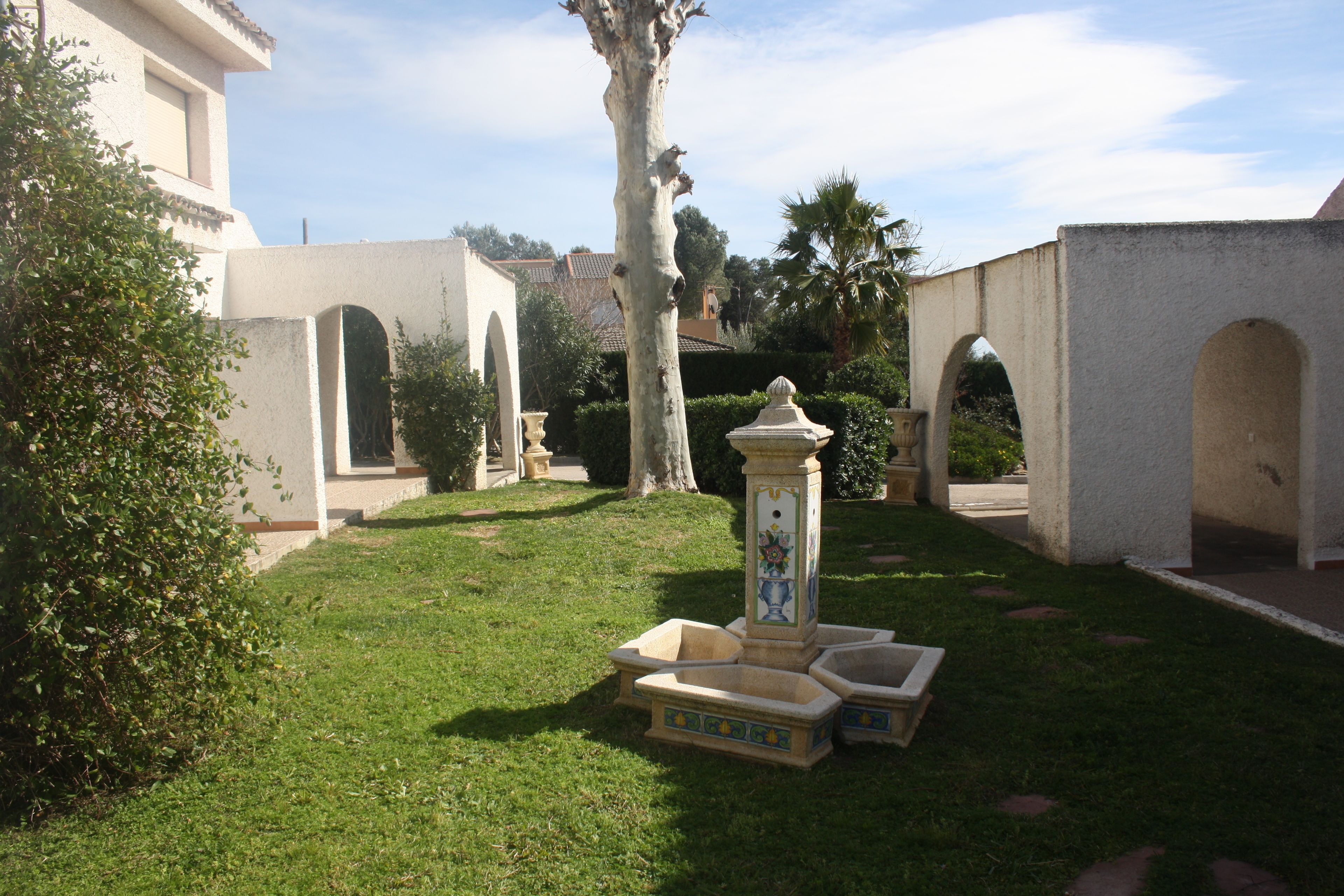 Un patio con una fuente, palmeras y un edificio con arcos.