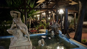 A nighttime outdoor area with a decorative fountain, a covered seating area, and a crowd of people. - Hotel La Carreta (Chiva)