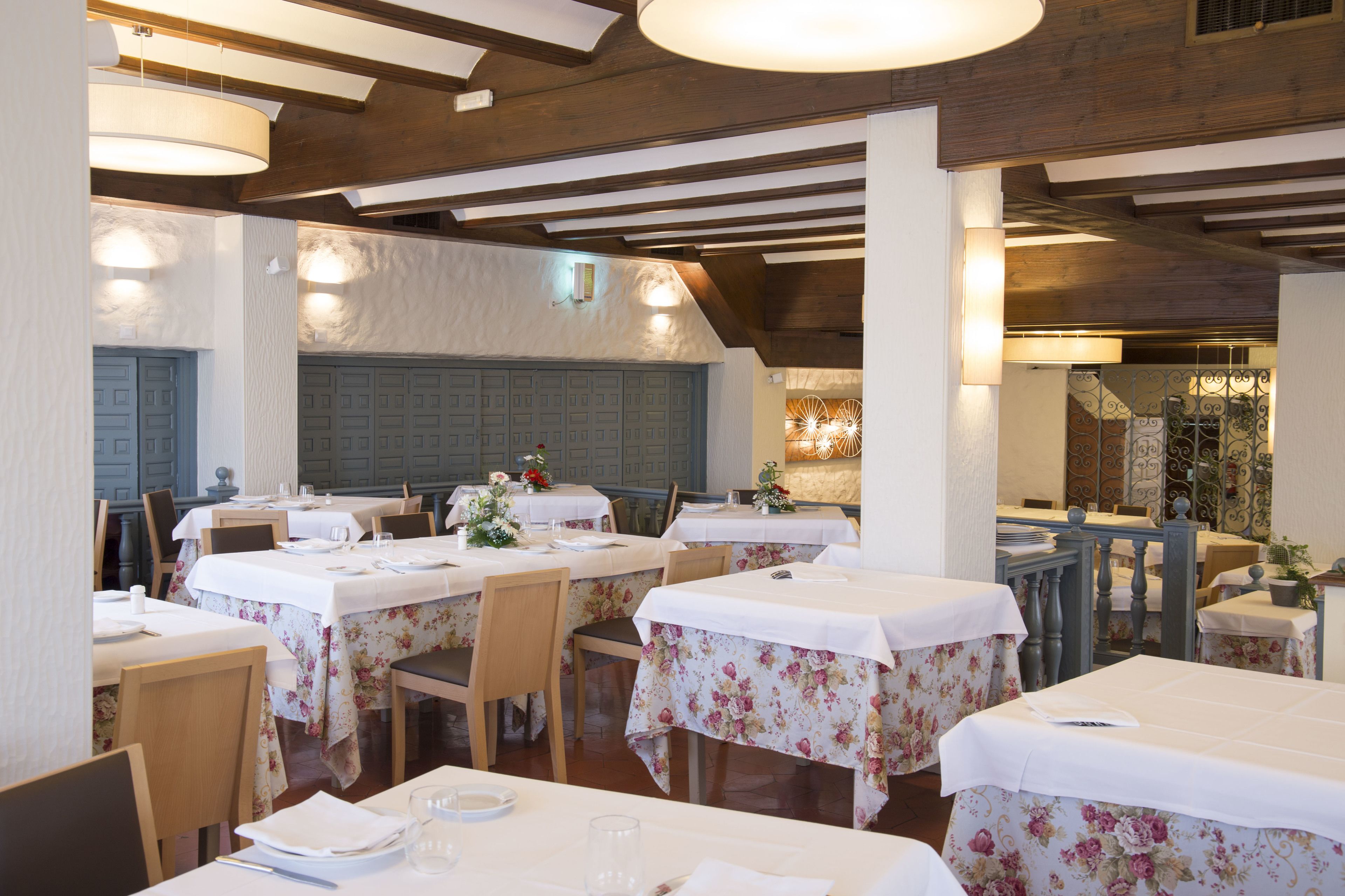 Un restaurante con varias mesas, vigas de madera en el techo y manteles florales.