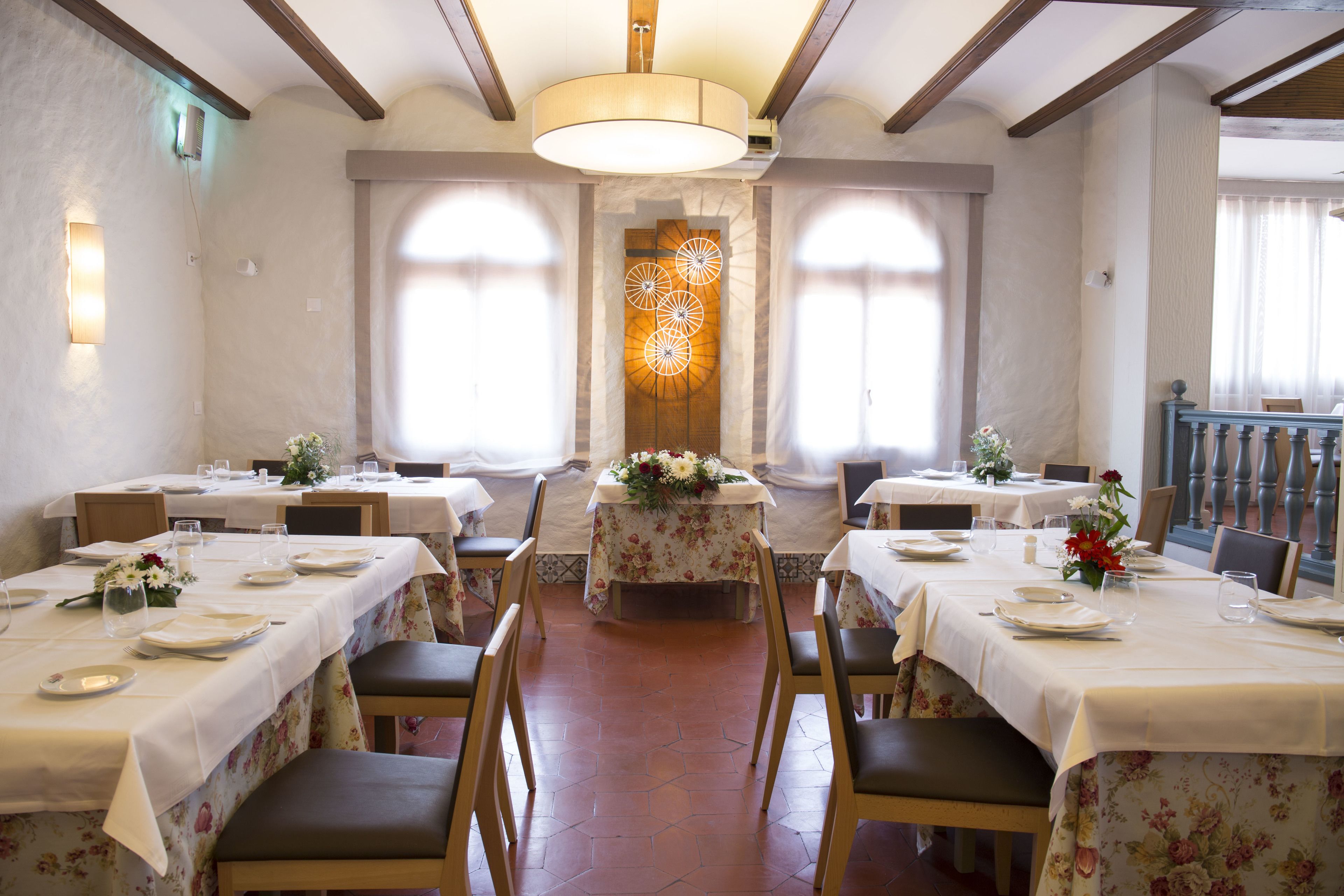Un espace repas avec des tables dressées pour le service, agrémenté d’un arrangement floral central et d’un lustre.