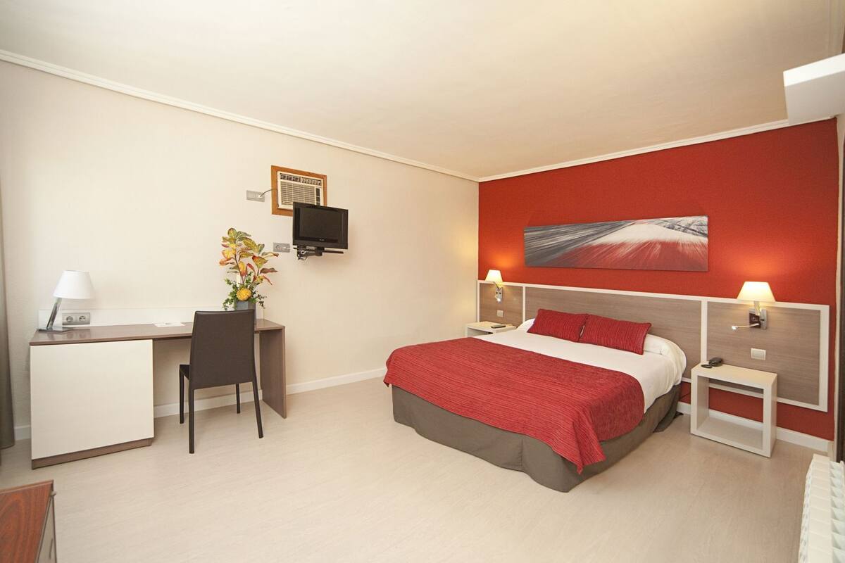 Una habitación de hotel con cama, escritorio, silla y televisor.