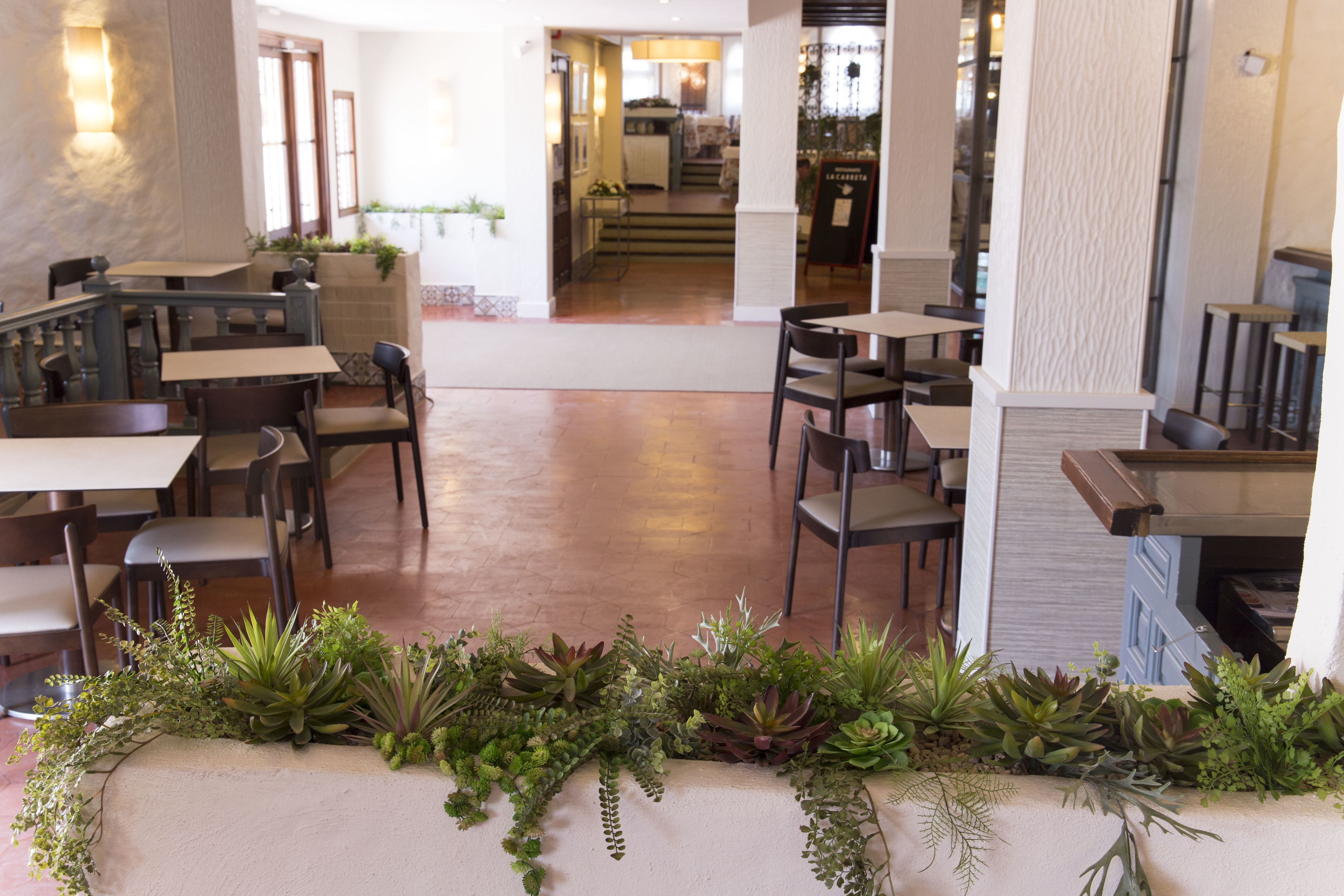 Un espacio interior amplio con varias mesas y sillas, un arreglo floral central y vistas a una zona de cocina.