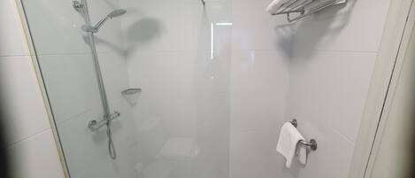 A glass-enclosed shower with a handheld showerhead, a fixed showerhead, and a handheld showerhead with a rain head.
