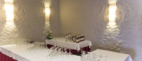 A banquet table with wine glasses and bottles, set against a textured wall with wall sconces.