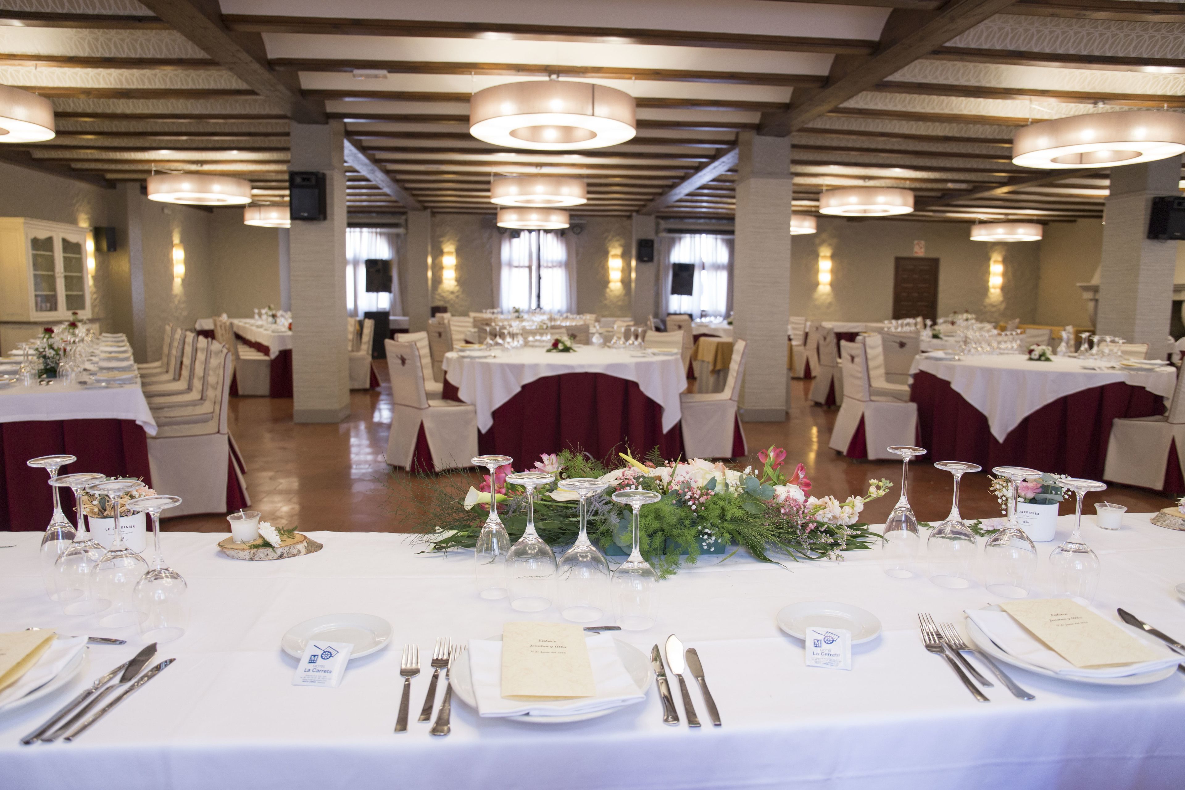 A banquet hall with multiple round tables set for dining, each with white tablecloths, chairs, and centerpieces.