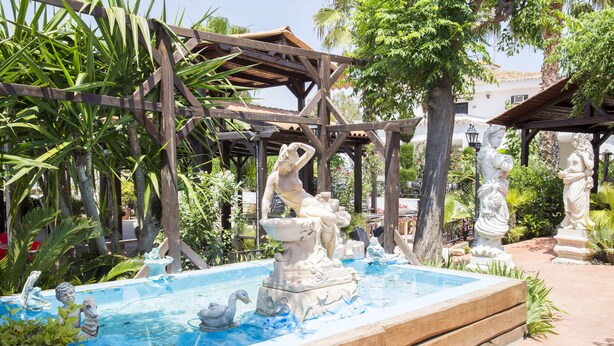 A garden with a fountain, statues, and a wooden pergola. - Hotel La Carreta (Chiva)